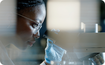 Scientist wearing gloves and glasses looking through a microscope.