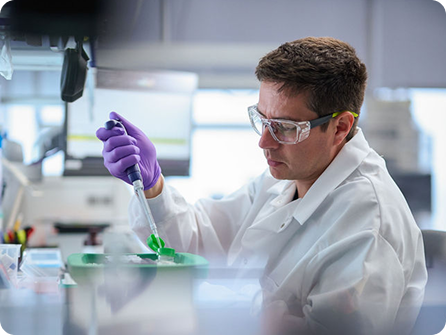 Scientist wearing goggles and gloves using a pipette in a laboratory.