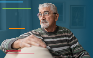 Older man with gray hair and glasses sitting on a couch, looking thoughtfully to the side.